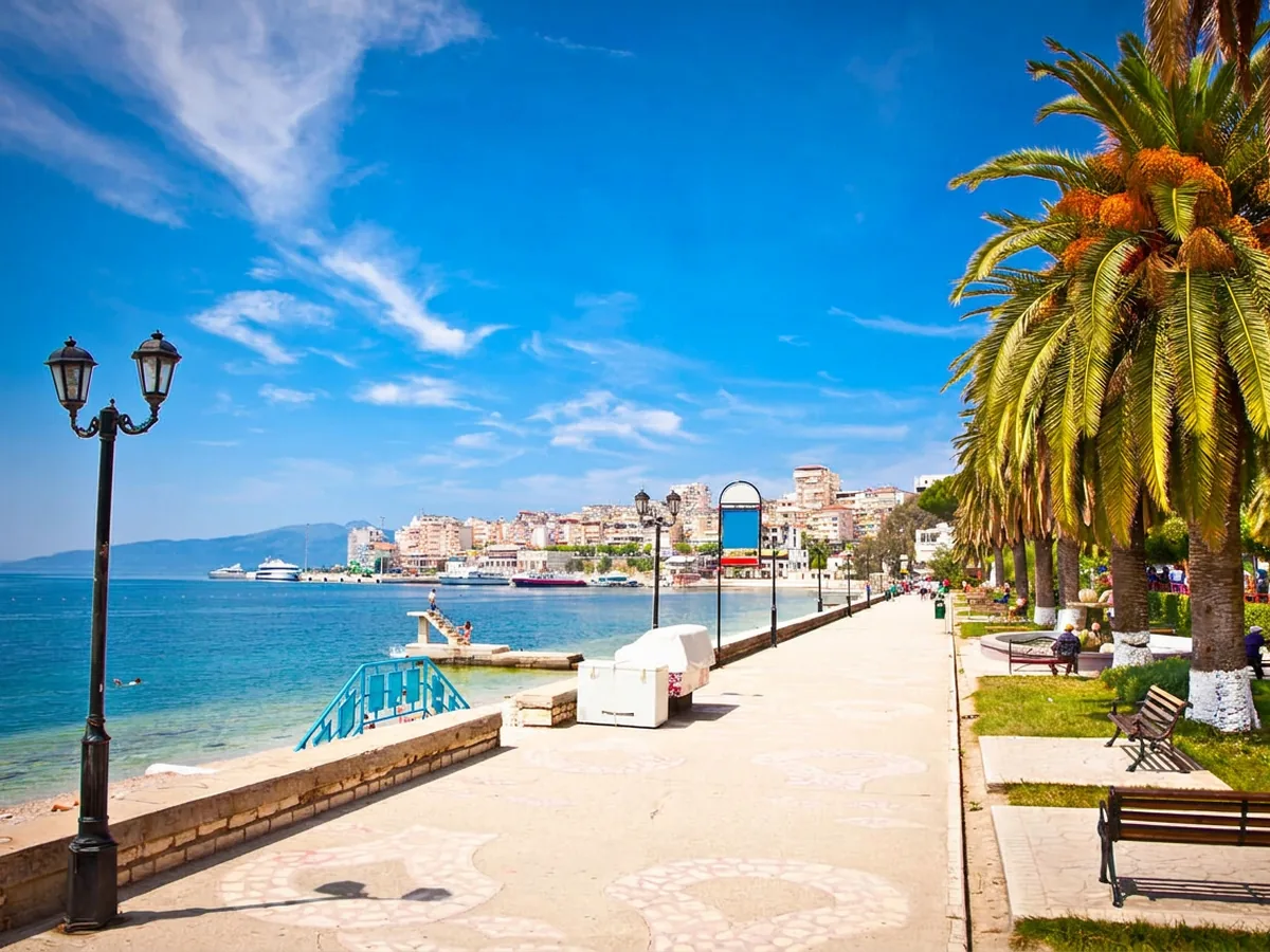 The seafront promenade in Saranda, palm-lined and full of evening walkers, with the bay behind.